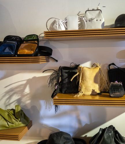 A collection of fashion bags and a hat displayed on wooden shelves in a boutique setting.